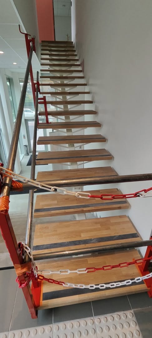 Escalier métallique blanc avec marches en bois et garde-corps vitré en cours de pose par ACPF dans une clinique à Marcq-en-Barœul